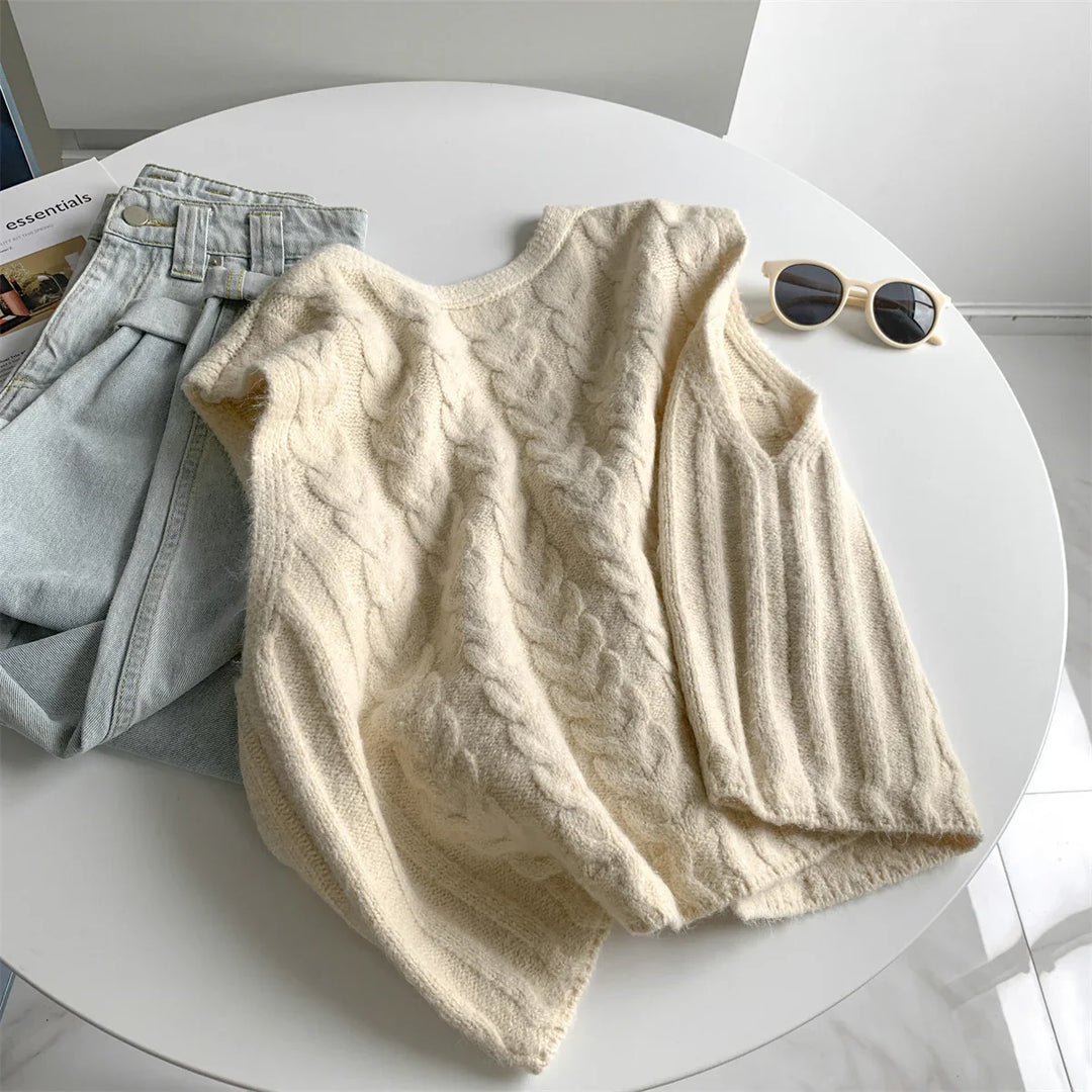Cozy cream cable knit sweater, light denim jeans, and beige sunglasses on white round table