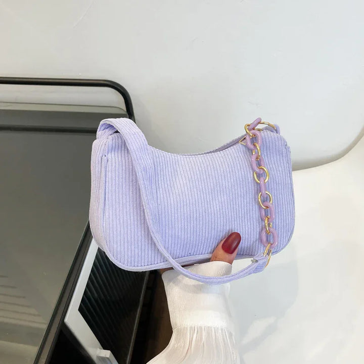 Light purple ribbed fabric shoulder bag with lavender and gold chain detail held by hand with red nails