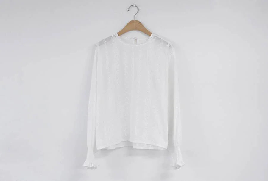 White long-sleeve lace blouse with ruffled cuffs on wooden hanger against plain white wall