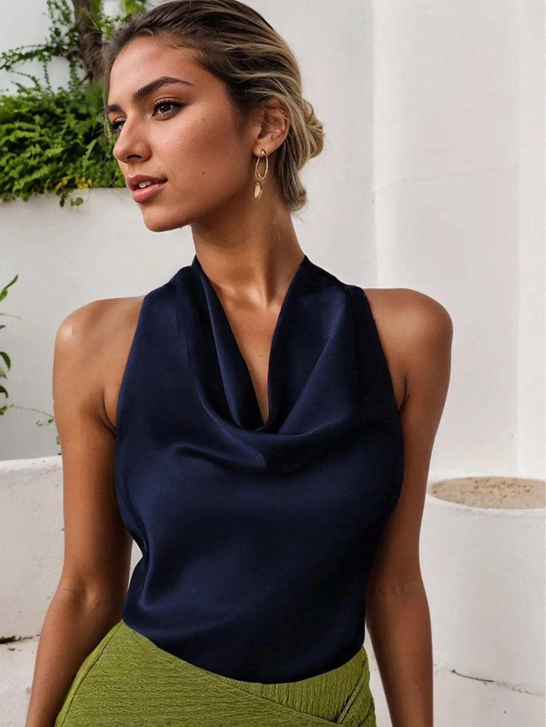 Woman in navy satin halter top and green textured skirt posing indoors with golden earrings and braided hair