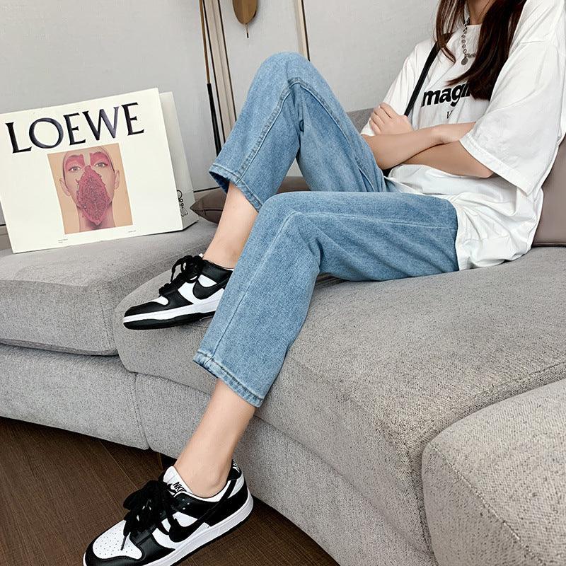 Person wearing black and white Nike sneakers and blue jeans sitting on a grey sofa with a LOEWE box in background