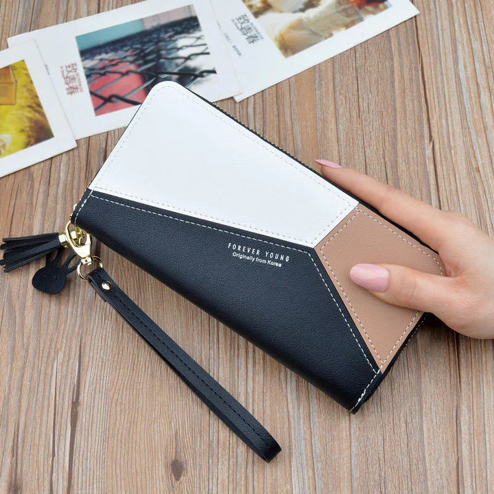 Hand holding a color-blocked leather wallet with wrist strap on wooden surface and photos