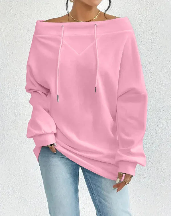 Woman wearing pink off-shoulder sweatshirt with drawstrings and light blue jeans against white wall