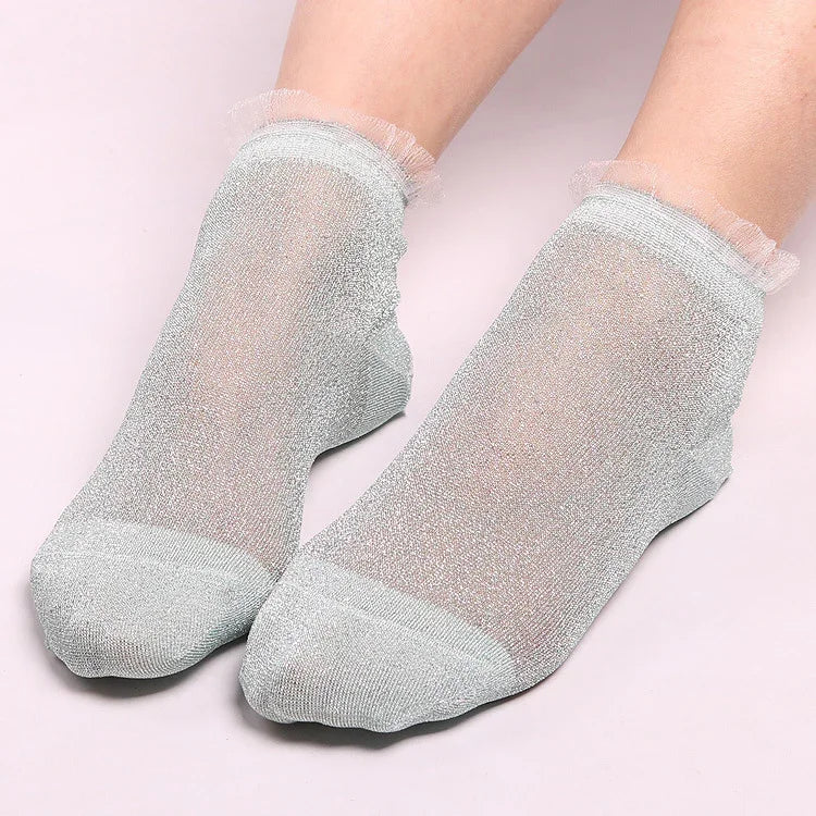 Close-up of feet wearing sheer silver glitter ankle socks with frilled cuffs on a light pink background