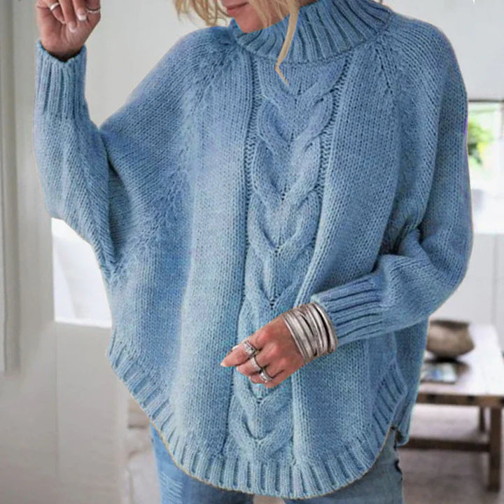 Woman wearing a cozy light blue chunky knit cable sweater with ribbed collar and cuffs indoors