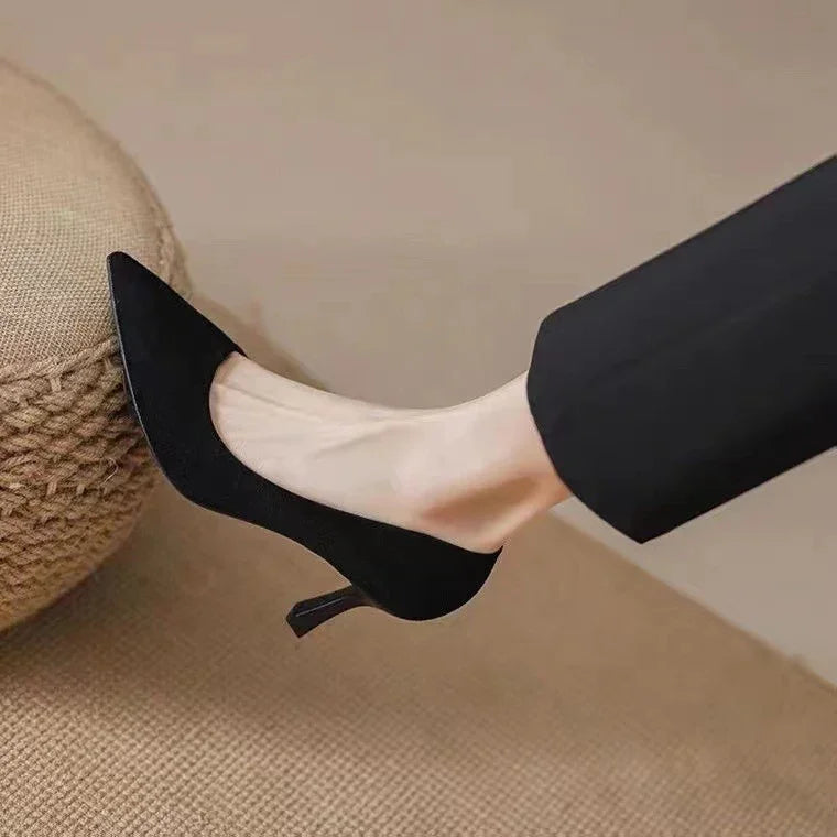 Close-up of foot wearing black pointed-toe kitten heel shoe with black pants, beige woven surface