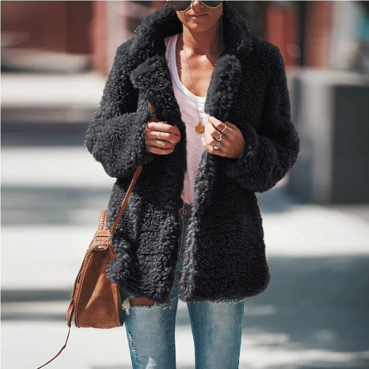 Woman wearing a black faux fur teddy coat, white t-shirt, ripped blue jeans, sunglasses, and brown crossbody bag outdoors