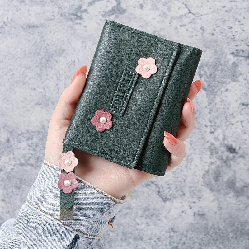 Hand holding dark green leather wallet decorated with pink flower appliques and pearl centers