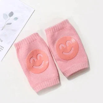 Pair of pink baby knee pads with smiley face design on white background