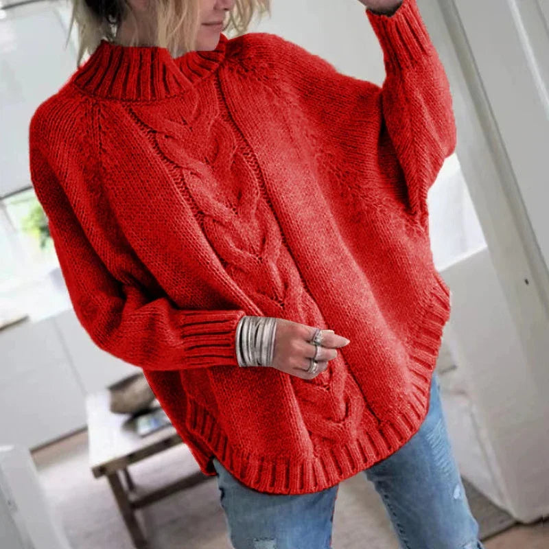 Woman wearing a bright red chunky cable knit sweater with ribbed collar and cuffs, paired with blue jeans indoors