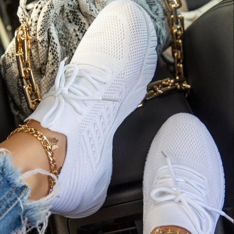 Close-up of white knitted sneakers worn with a gold chain anklet and distressed jeans inside a car