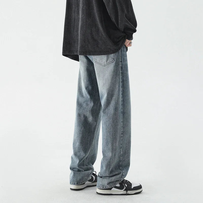 person wearing loose faded blue jeans and black and white sneakers against white background
