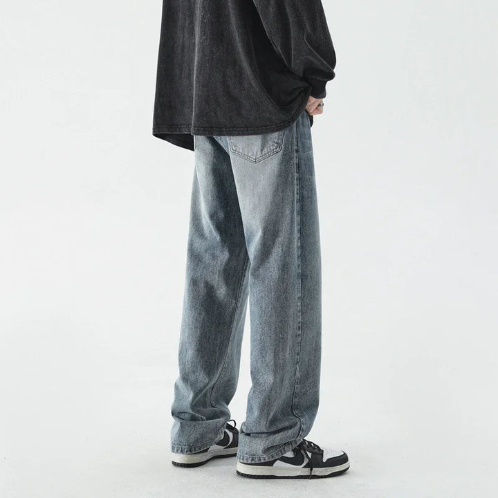 person wearing loose faded blue jeans and black and white sneakers against white background