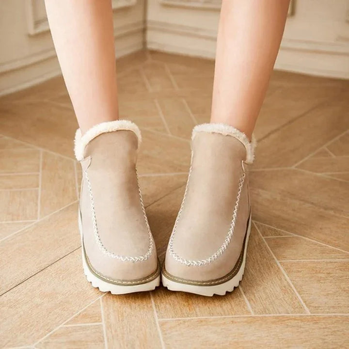 Beige winter boots with white fur trim and thick white soles worn on wooden floor