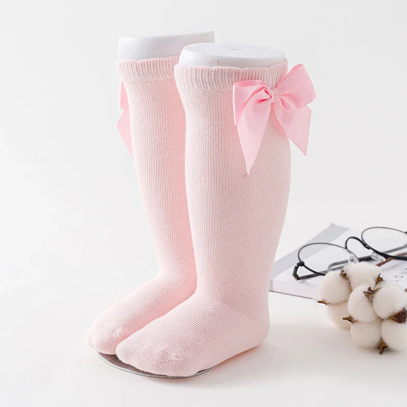 Pair of soft pink baby knee-high socks with decorative bows on a white background