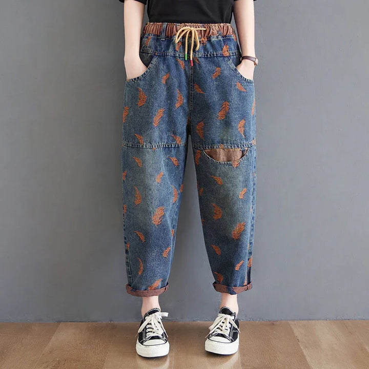 Woman wearing loose denim pants with orange leaf prints, elastic waistband, rolled cuffs, and black sneakers