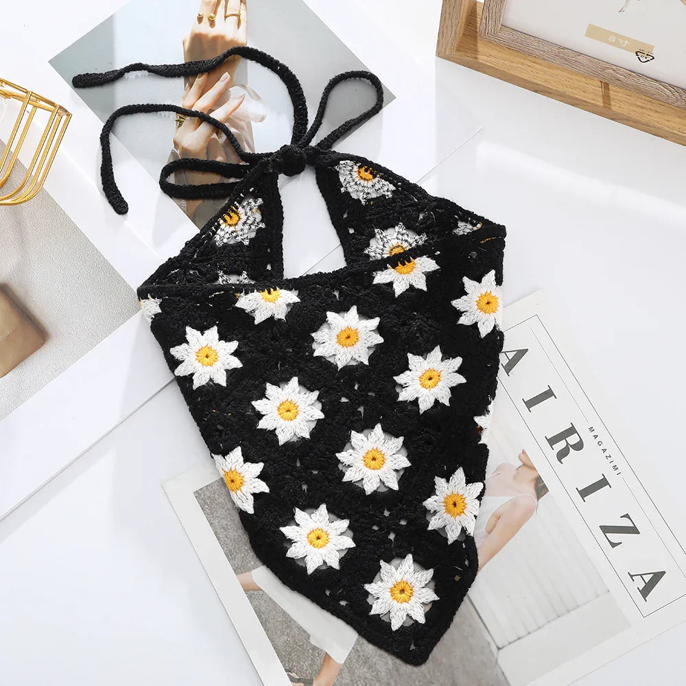 Black crochet halter top with white and yellow daisy flower patterns on a white table with magazines