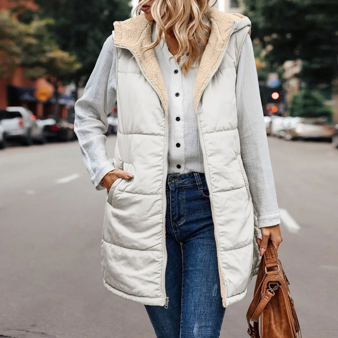 Woman wearing a white sherpa-lined sleeveless puffer vest, white blouse, blue jeans, carrying brown leather bag