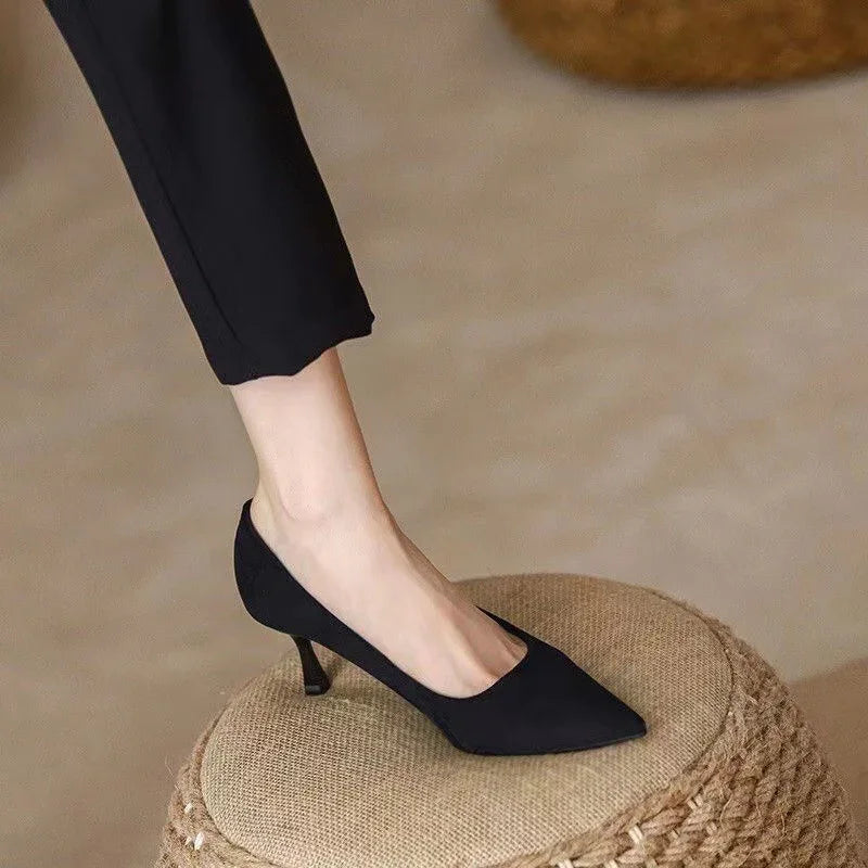 Woman wearing black pointed-toe kitten heel shoes standing on woven beige ottoman