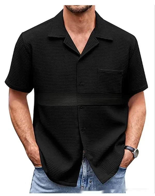 Man wearing black textured short-sleeve button-up shirt with chest pocket and blue jeans