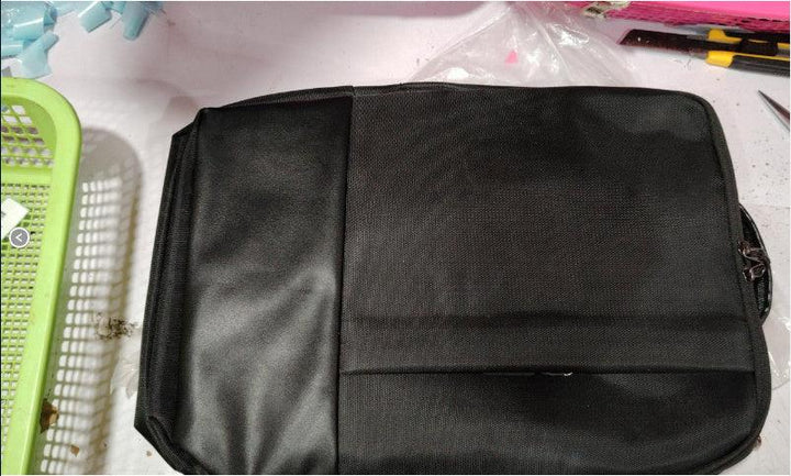 Black rectangular laptop bag with textured and smooth panels on a white table with tools and green basket