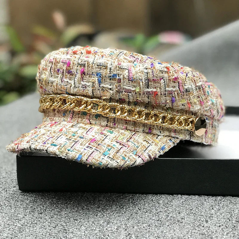 Multicolor tweed baker boy hat with gold chain detail on black box, outdoor background