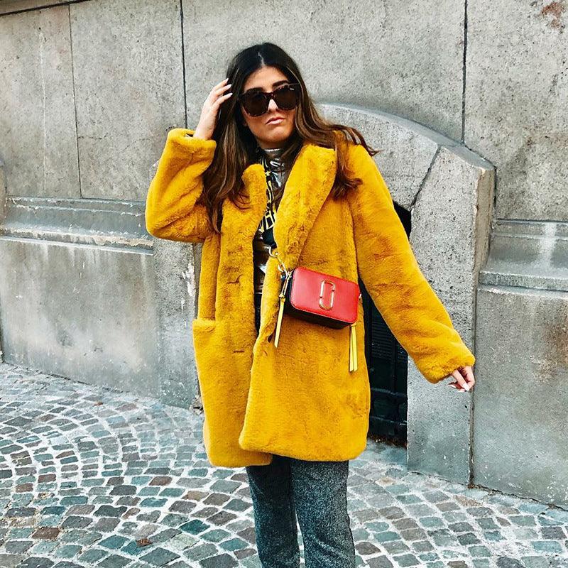 Woman in a bright yellow faux fur coat with a red crossbody bag and sunglasses on cobblestone street