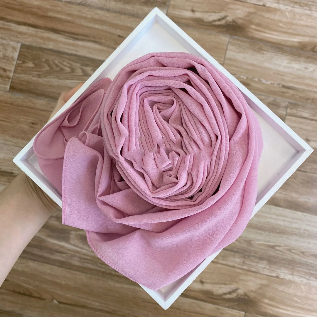 Hand holding a white square box with neatly rolled pink chiffon fabric on wooden floor
