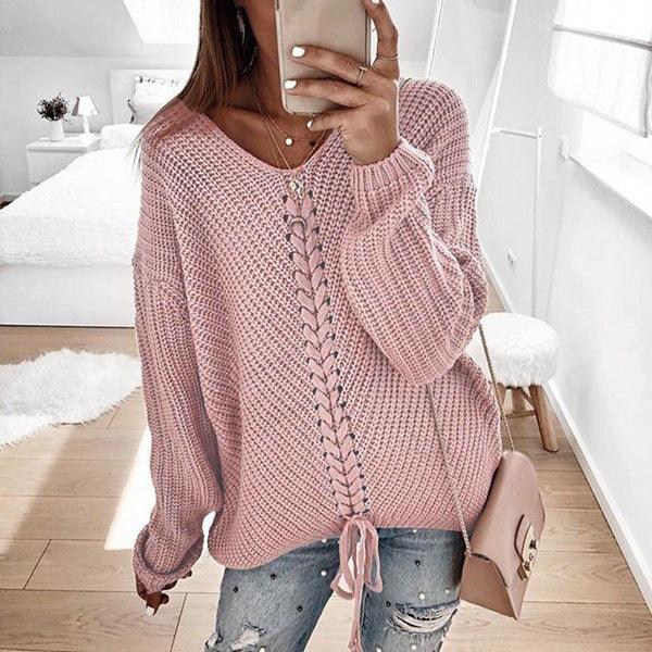 Woman wearing a pink chunky knit sweater with lace-up front and ripped jeans in a bright modern bedroom