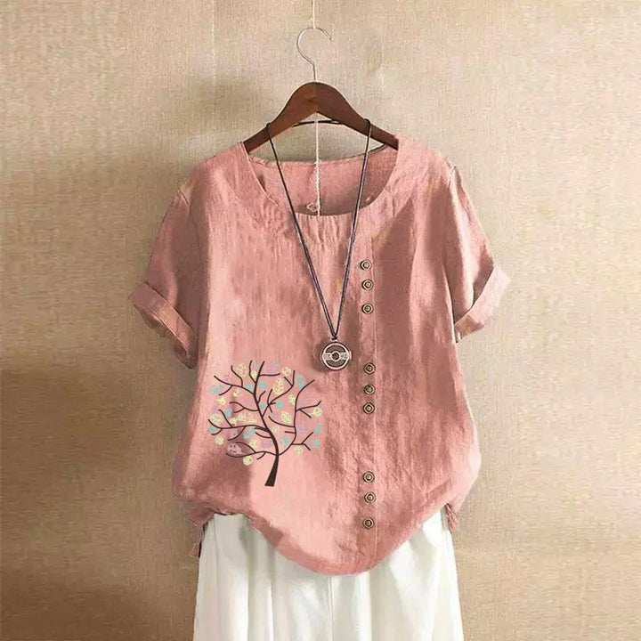 Pink short-sleeve blouse with tree design and button details, paired with white pants on hanger