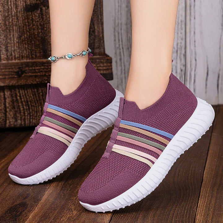 Purple knitted slip-on sneakers with multicolor stripes and white soles on wooden floor