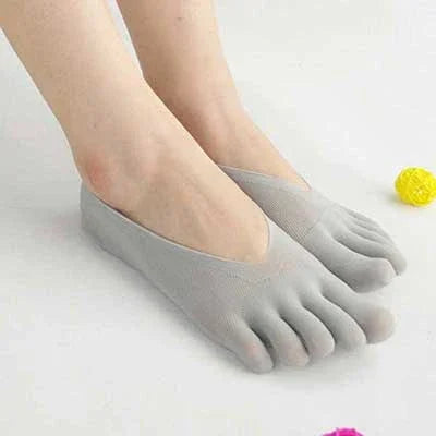 Feet wearing light gray toe socks on a white surface with small colorful decorative balls