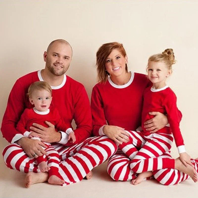 Happy family of four in matching red and white striped Christmas pajamas against beige background