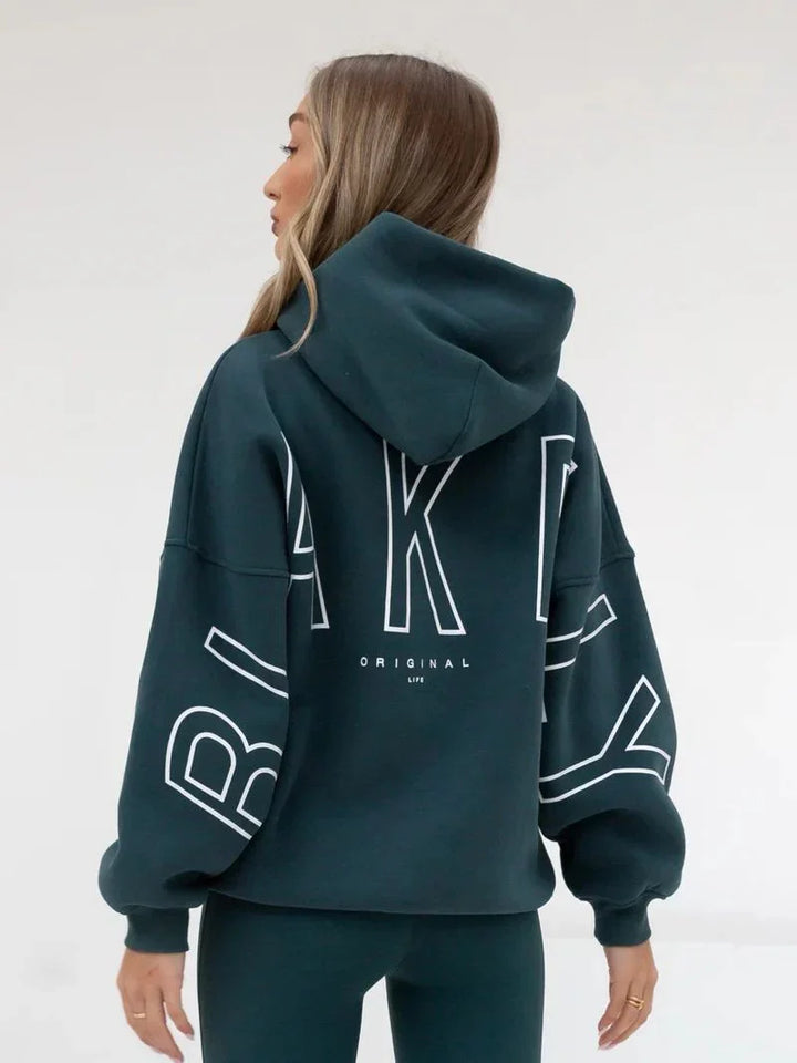 Woman wearing dark teal oversized hoodie with white block letters and matching leggings in studio