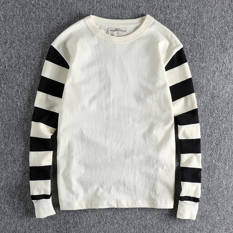 White long-sleeve knit sweater with black horizontal stripes on sleeves laid on gray fabric