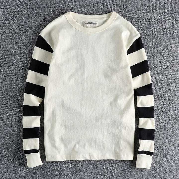 White long-sleeve knit sweater with black horizontal stripes on sleeves laid on gray fabric