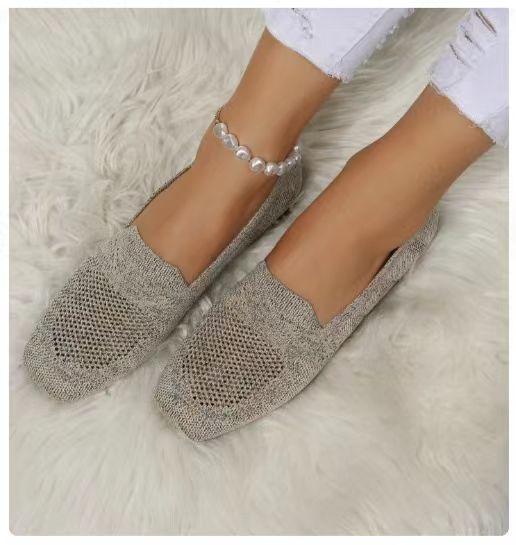 Feet wearing knitted beige slip-on shoes and white ripped jeans, with a pearl ankle bracelet on a fluffy white rug