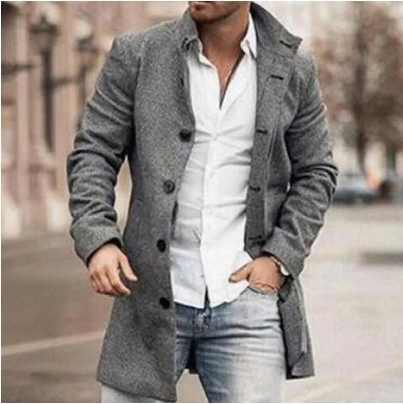 Man wearing grey wool coat over white shirt and blue jeans walking in urban street setting
