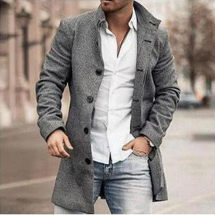Man wearing grey wool coat over white shirt and blue jeans walking in urban street setting