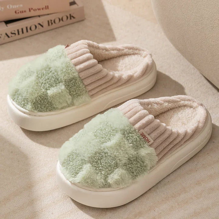 Pair of cozy green and beige plush indoor slippers with thick white soles on carpet