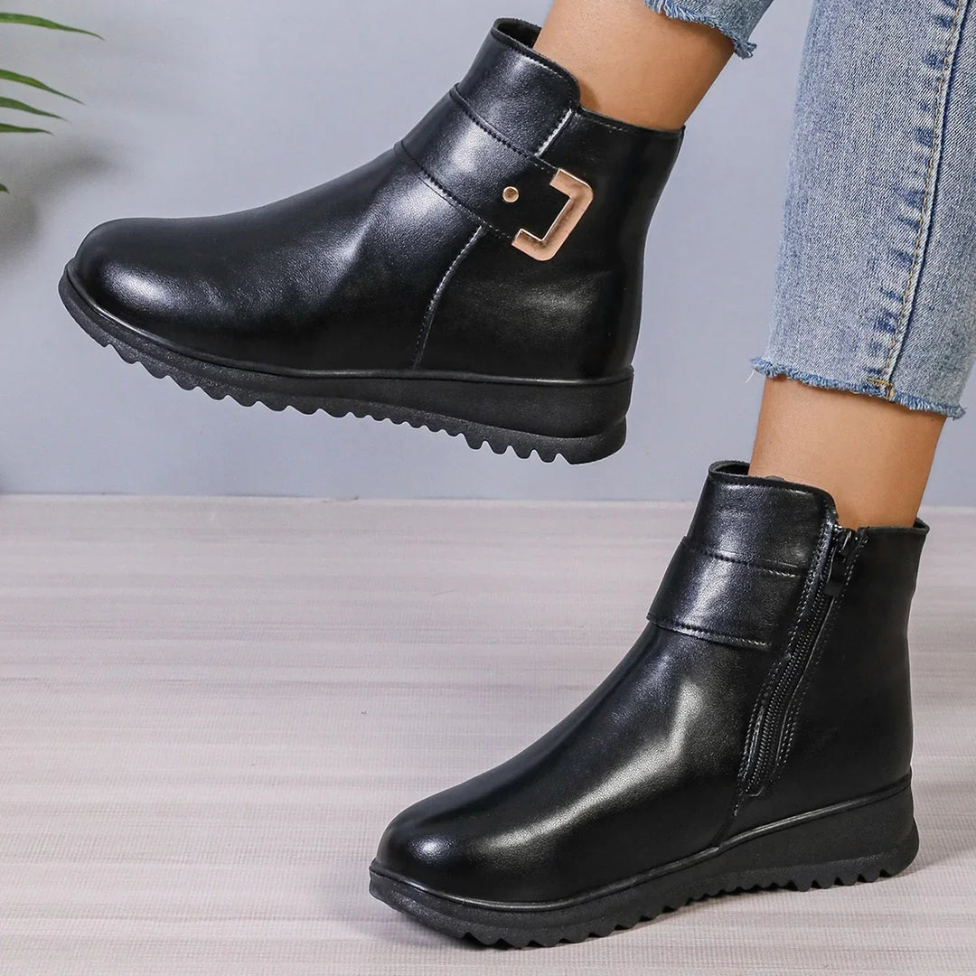 Black leather ankle boots with side zipper and gold buckle detail worn with cropped denim jeans