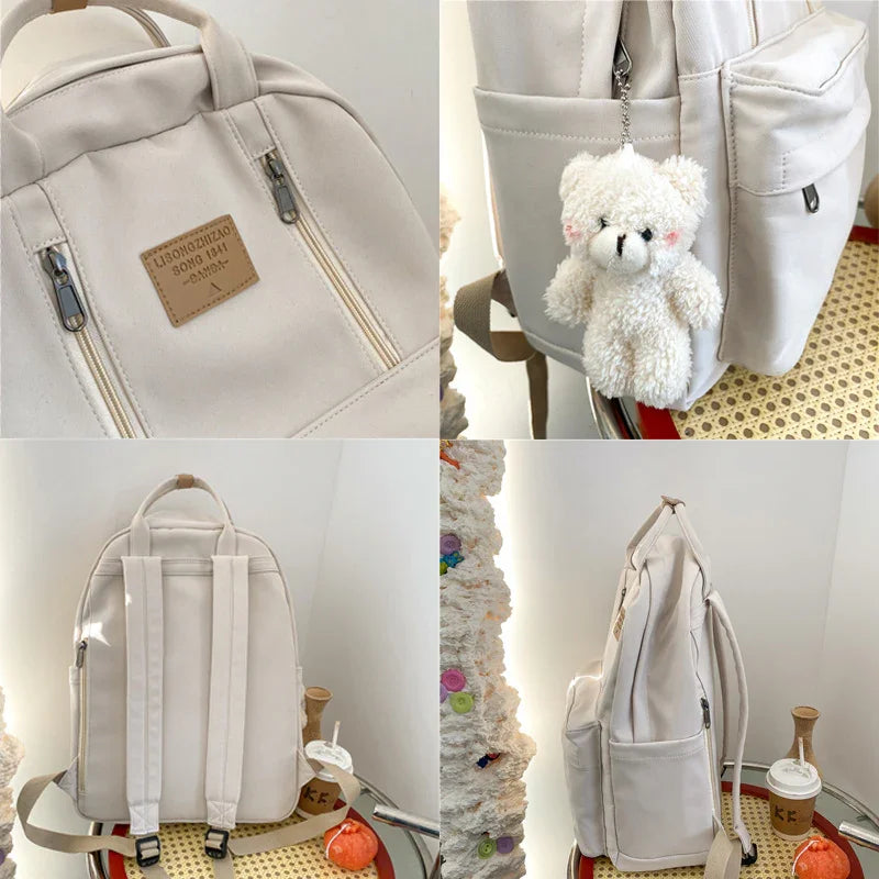 Cream white canvas backpack with front zippers and plush teddy keychain hanging on side pocket