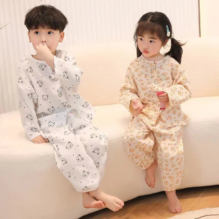 Two children in cozy printed pajamas sitting on a white sofa, one with bear prints and one with floral pattern