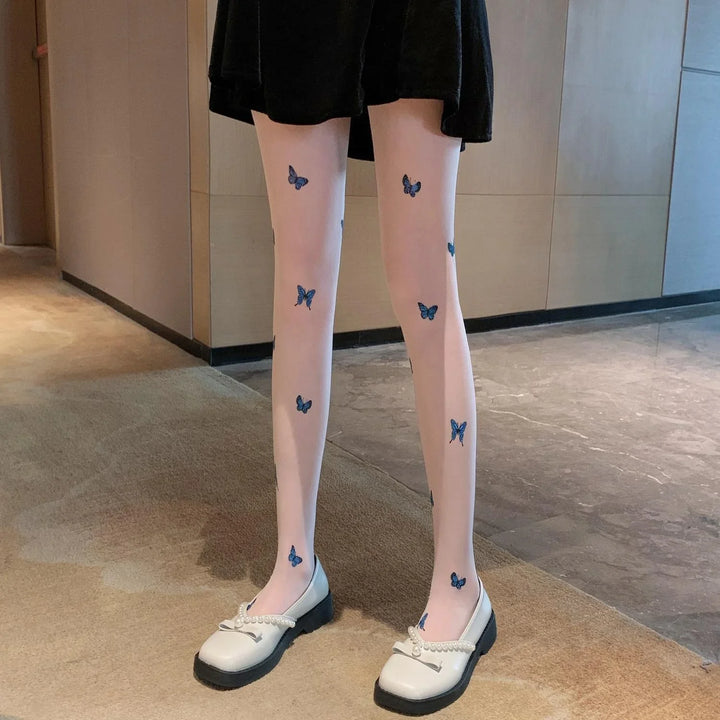Legs wearing sheer tights with blue butterfly prints paired with white pearl-decorated loafers