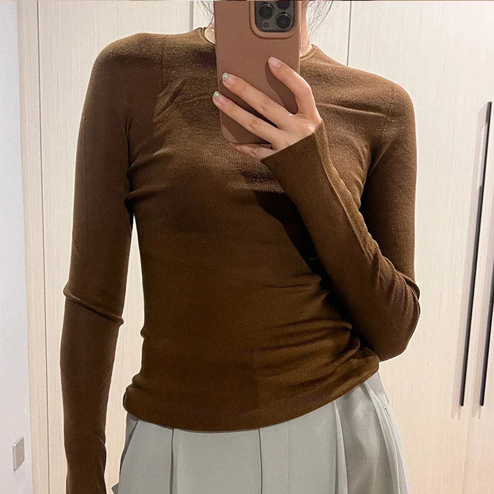 Person wearing a fitted brown long-sleeve top and light grey pleated pants, taking a mirror selfie