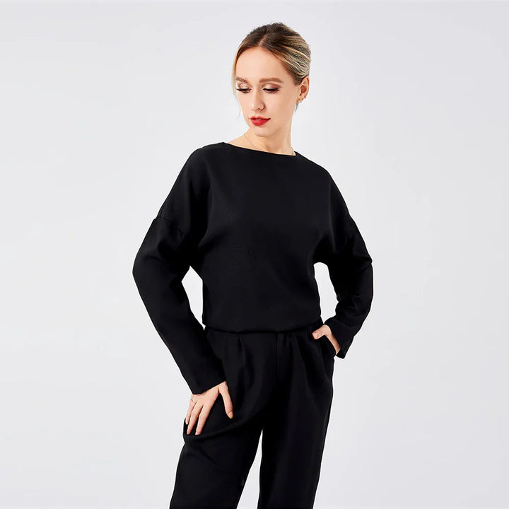 woman in black long-sleeve top and pants posing against white background