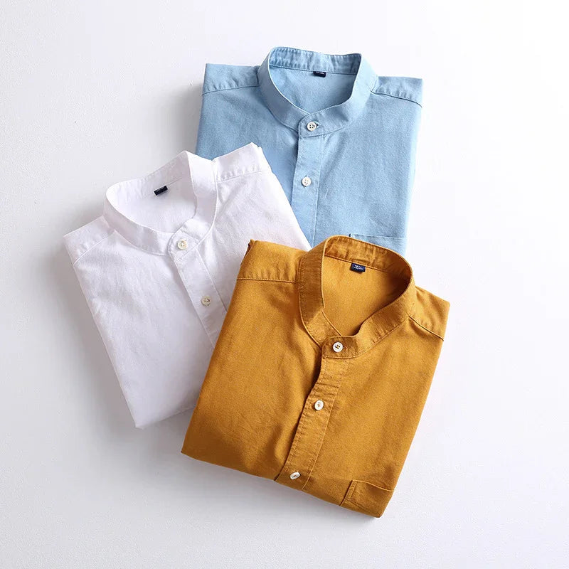 Folded mandarin collar shirts in blue, white, and mustard yellow on white background