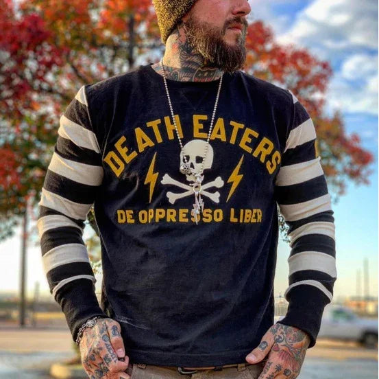 Bearded man wearing a black Death Eaters shirt with skull and crossbones design, striped sleeves, and fall trees in background