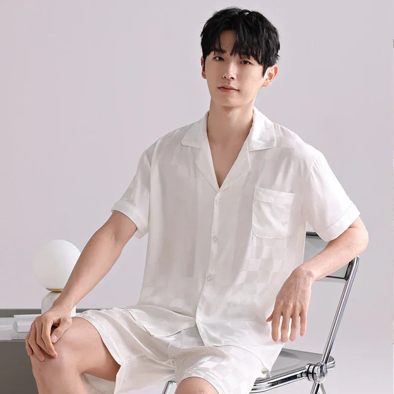 Young man wearing white checkered satin short-sleeve pajamas sitting on metal chair in minimal room