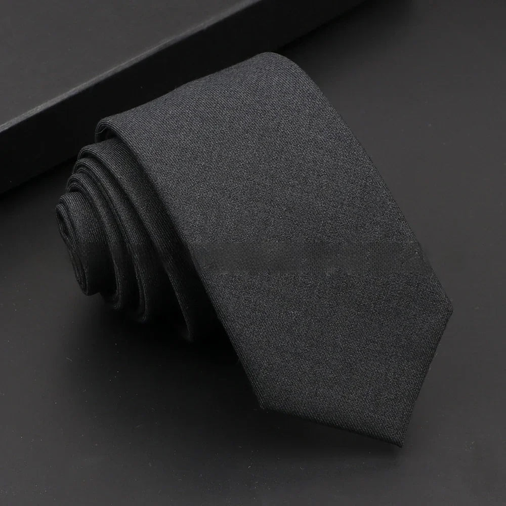 Rolled black plain silk tie on black background with matching black gift box